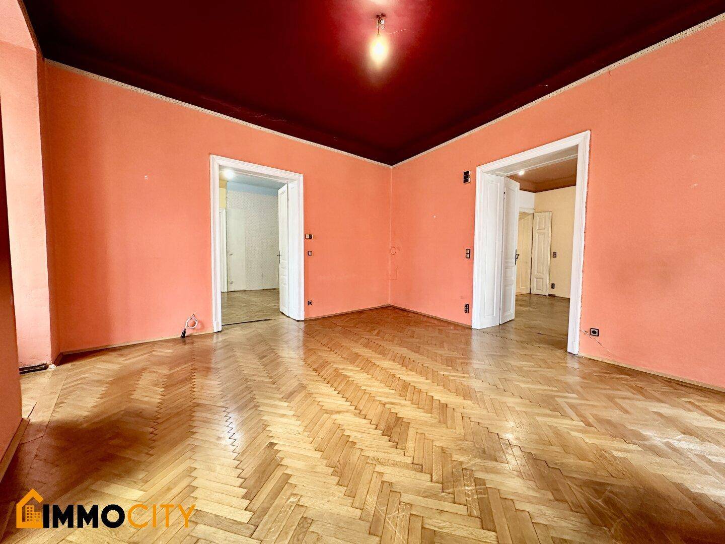 Großes Zimmer mit Fischgrätparkett, farbigen Wänden und Decke, sowie zwei breiten Türöffnungen.