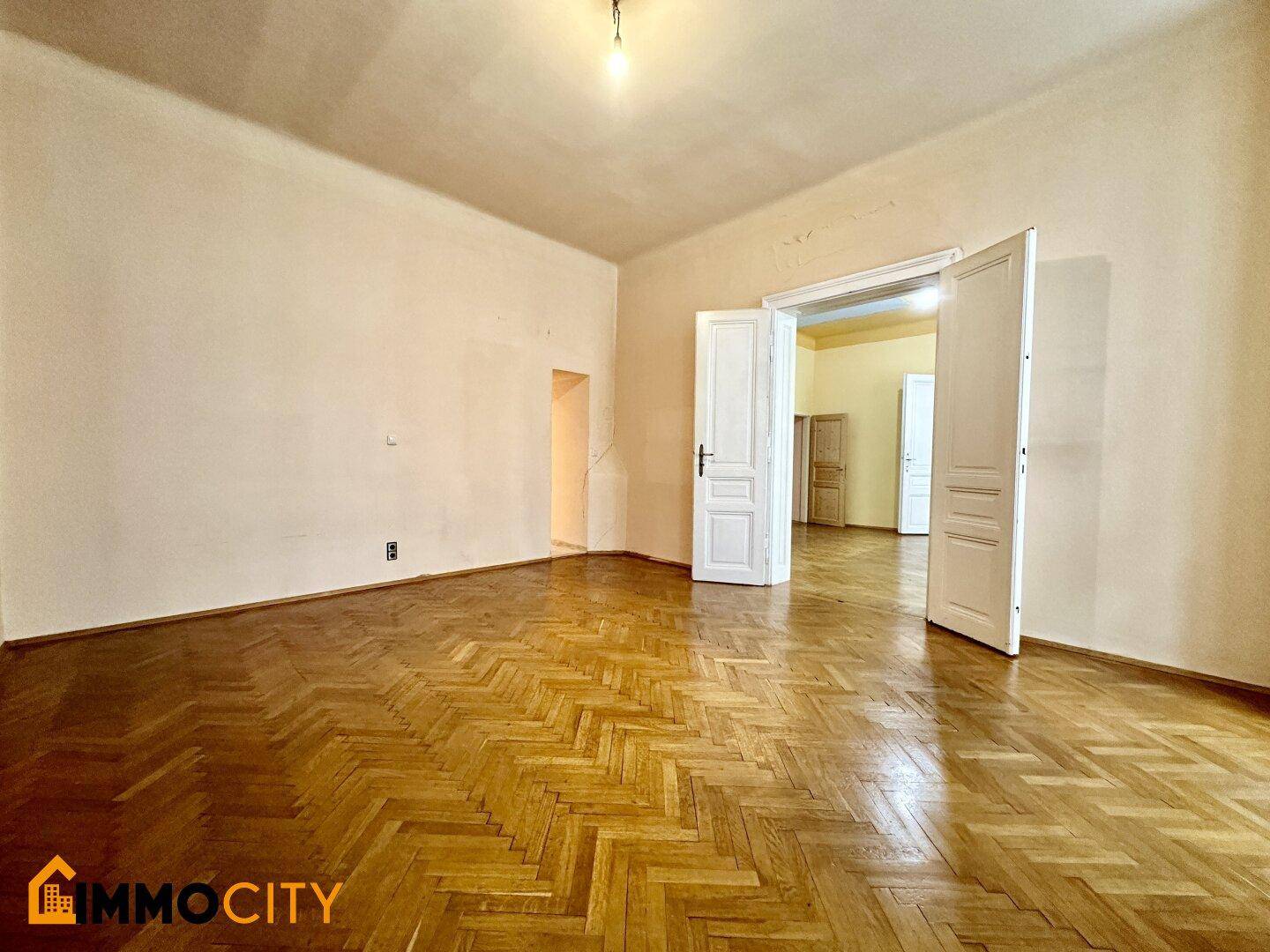 Geräumiges Zimmer mit Fischgrätparkett und hohen Decken, mit Blick in angrenzende Räume.