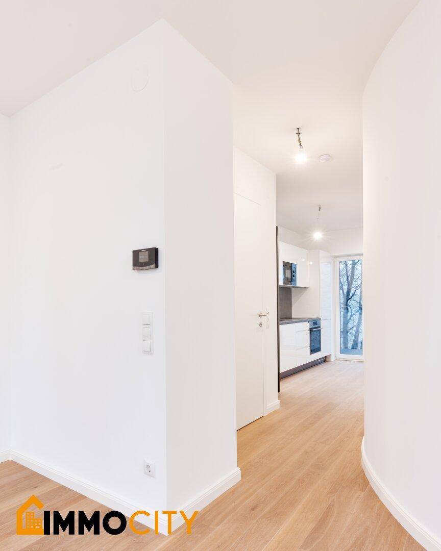 Heller Flur mit Holzboden, der zum Küchenbereich und Balkon führt.