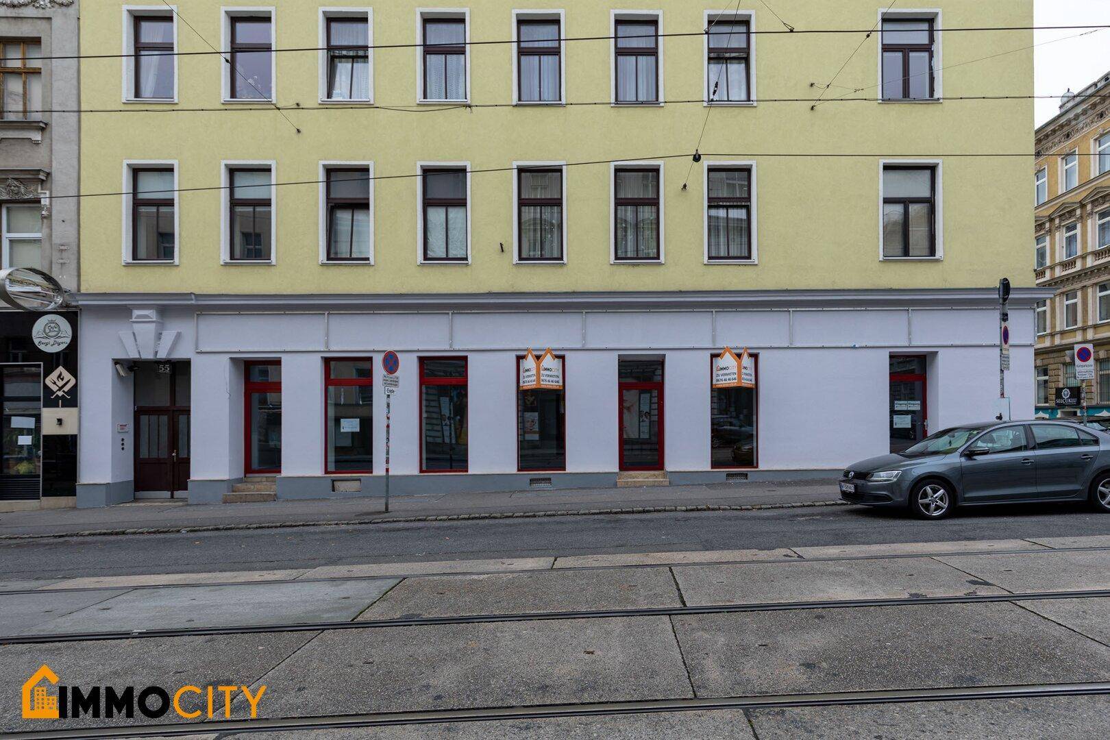 Nahaufnahme der gelben Fassade eines Stadthauses mit großen Schaufenstern im Erdgeschoss und Straßenbahnlinien.