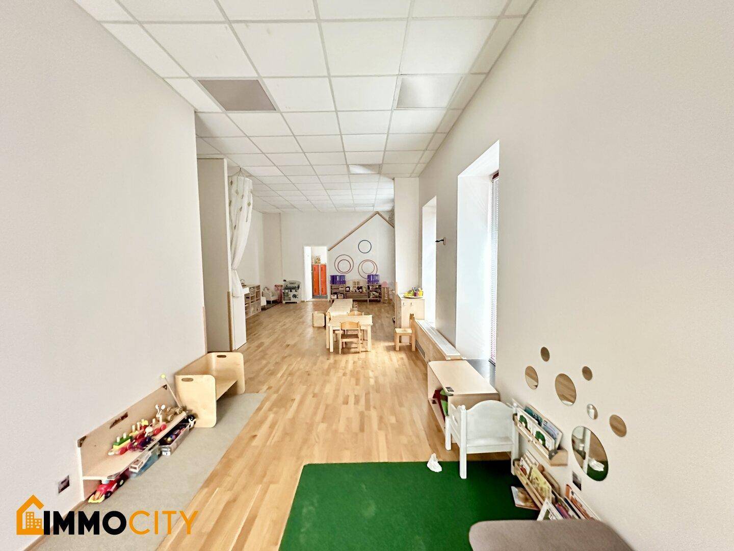 Heller Spielraum mit Holzboden, Kindermöbeln und einem grünen Teppichbereich, gut organisiert.