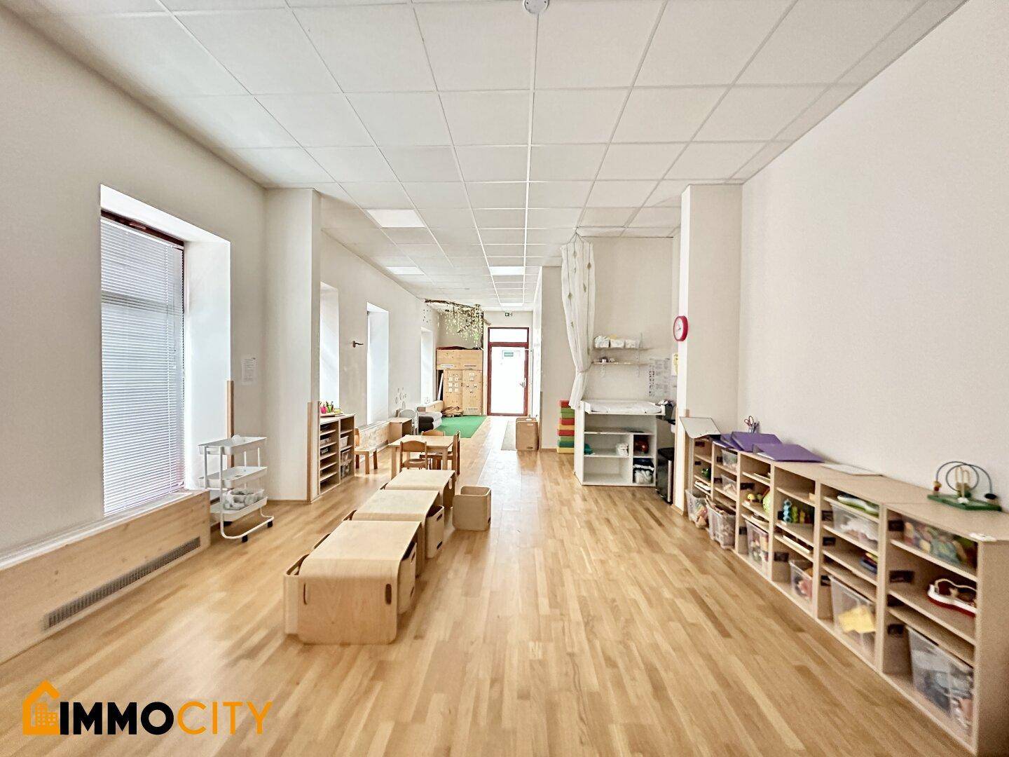 Weitläufiger Spielbereich mit Holzboden, Kindermöbeln und einem Wickeltisch, ideal für eine Kindertagesstätte.