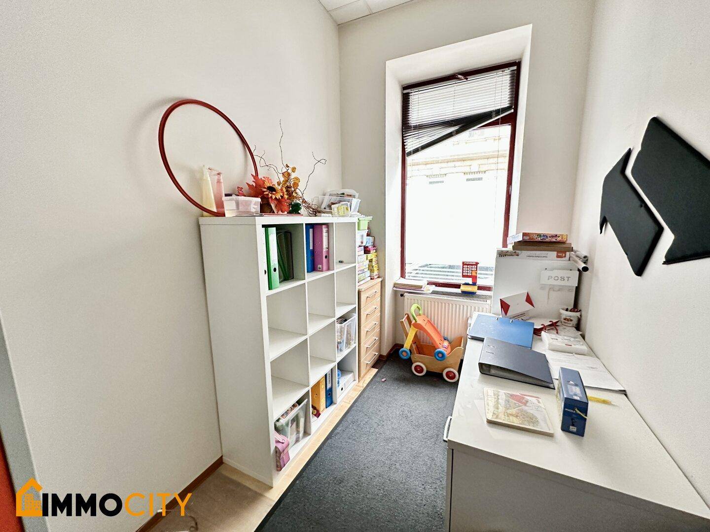 Kleines Büro mit Schreibtisch, Regal und Fenster, ideal für Verwaltungsaufgaben in der Einrichtung.