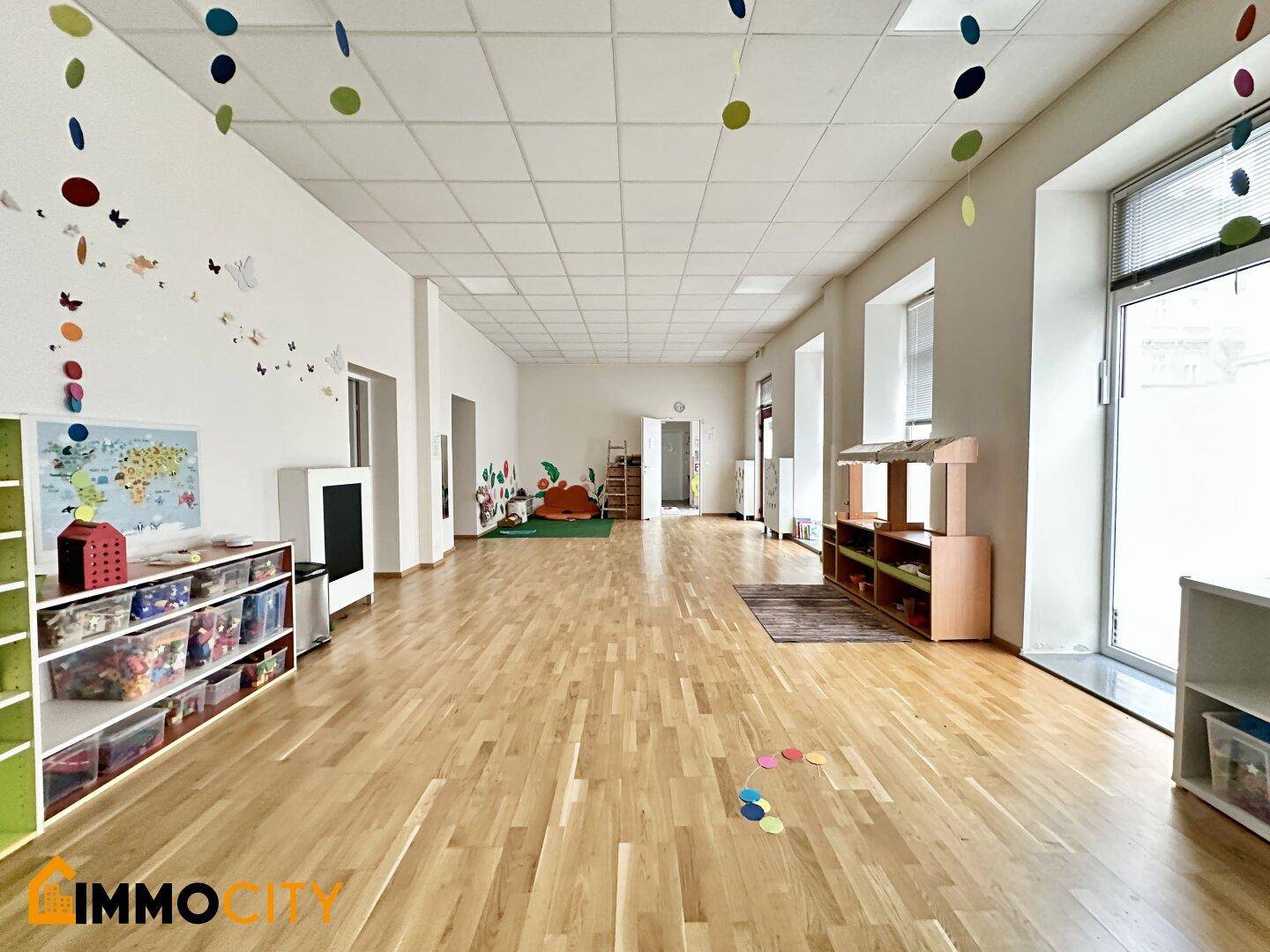 Weitläufiger Spielbereich mit Holzboden, bunten Dekorationen und Regalen, ideal für Kinderaktivitäten.