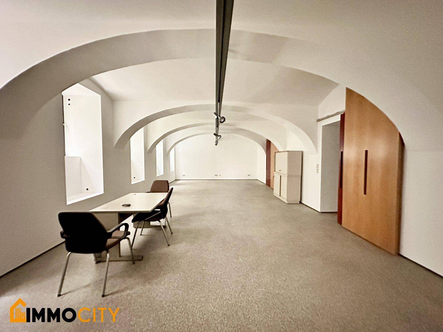 Großer Raum mit Gewölbedecken, Teppichboden und mehreren Fenstern, ideal für Büros oder Ausstellungen.