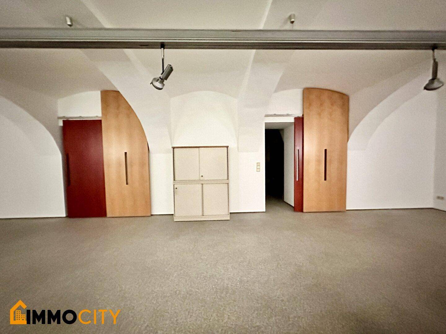 Geräumiger Raum mit Gewölbedecken, Terrazzoboden und großen Schiebetüren aus Holz.