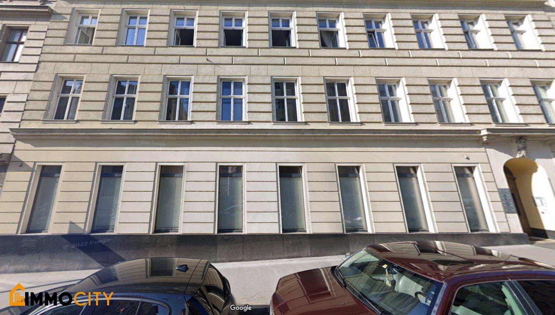Klassische Fassade eines Mehrfamilienhauses mit vielen Fenstern und geparkten Autos davor.