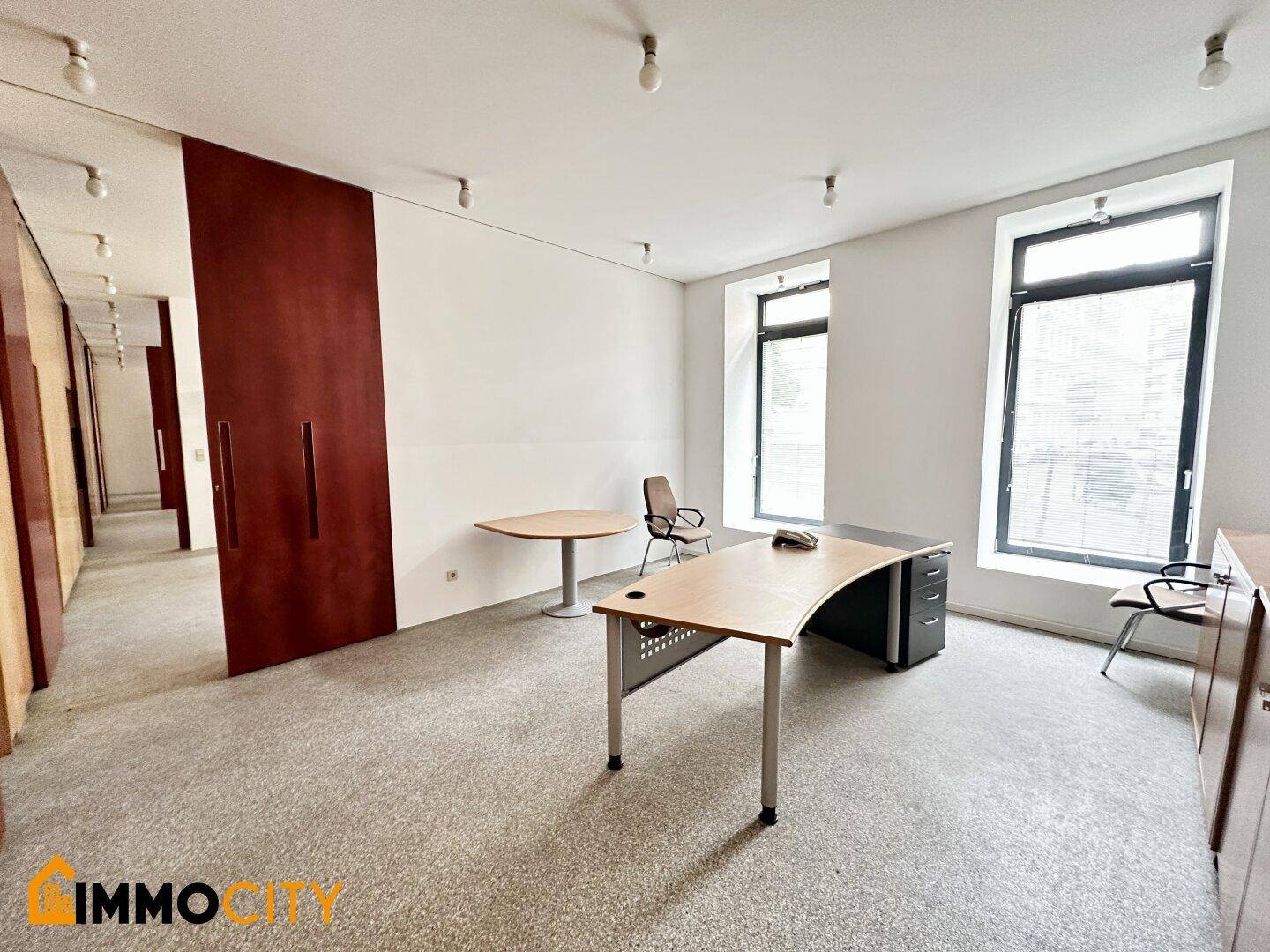 Langes Büro mit Teppichboden, modernen Schreibtischen und modularen Holzschiebetüren entlang der Wand.