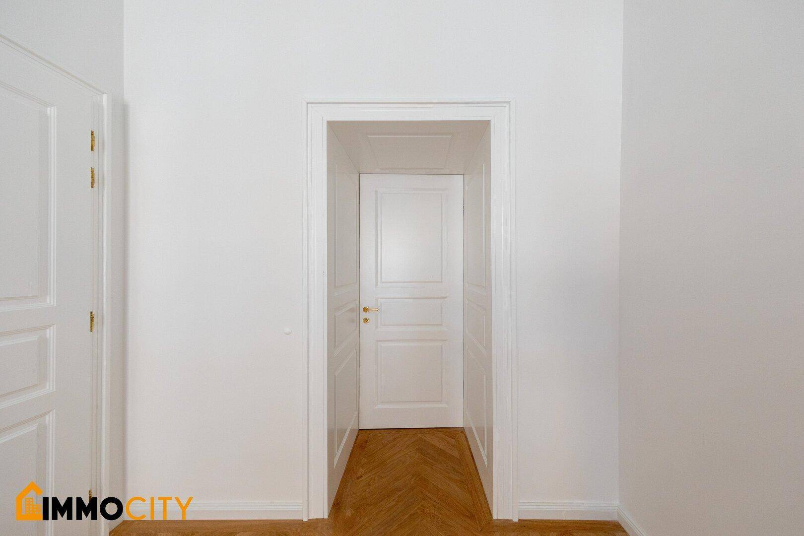 Heller Durchgangsbereich mit Fischgrätparkett und einer weißen Tür, die zu einem weiteren Zimmer führt.