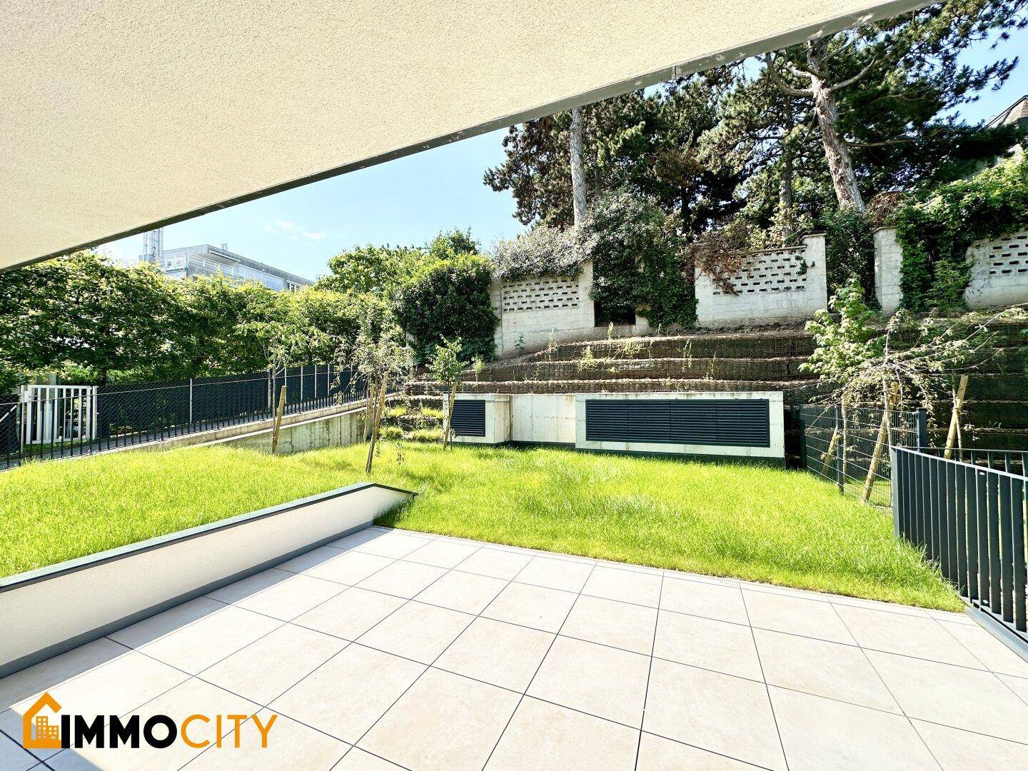 Überdachte Terrasse mit Fliesenboden und Zugang zu einem privaten Gartenbereich mit Rasen.