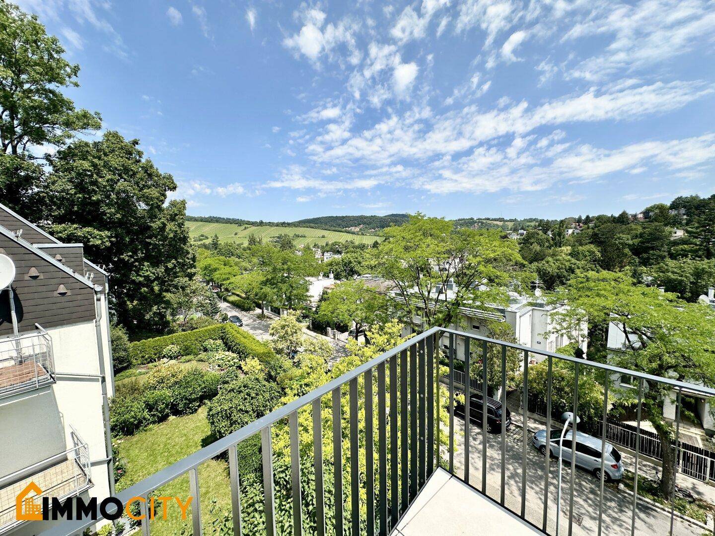 Balkon mit Metallgeländer und Blick auf die Straße, Bäume und umliegende Häuser.