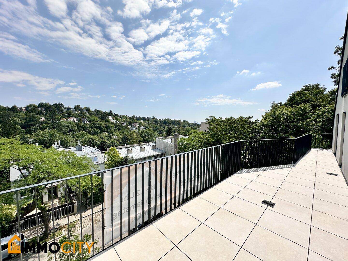 Helle, geflieste Terrasse mit minimalistischer Brüstung und Ausblick auf die bewaldete Umgebung.