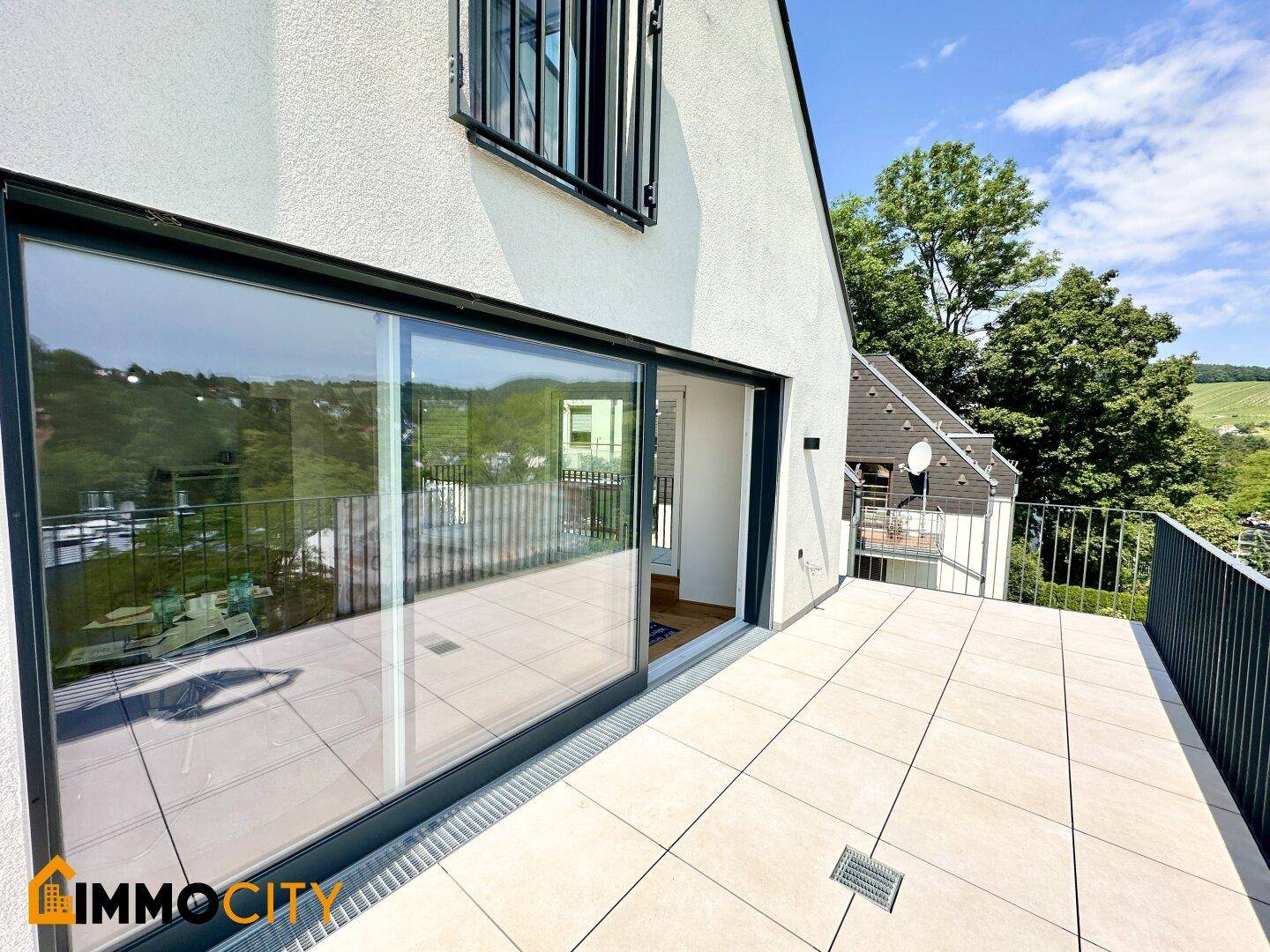 Große Glasschiebetüren führen von den Innenräumen auf die weitläufige, geflieste Terrasse.