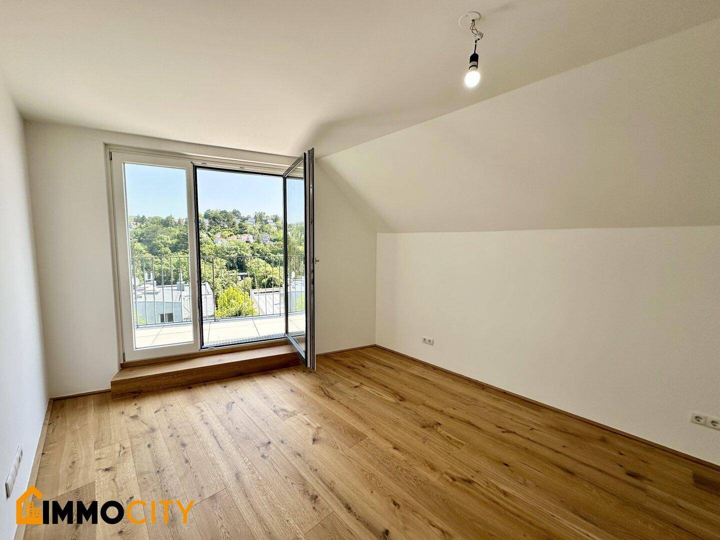 Helles Dachgeschosszimmer mit Holzboden, Dachschräge und französischem Balkon mit Ausblick.