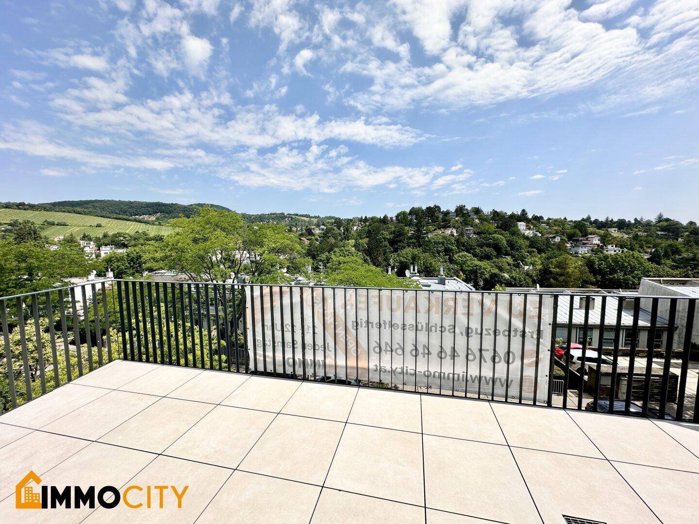 Sonnige Terrasse mit beigem Fliesenboden und weitem Blick über die grüne Landschaft.