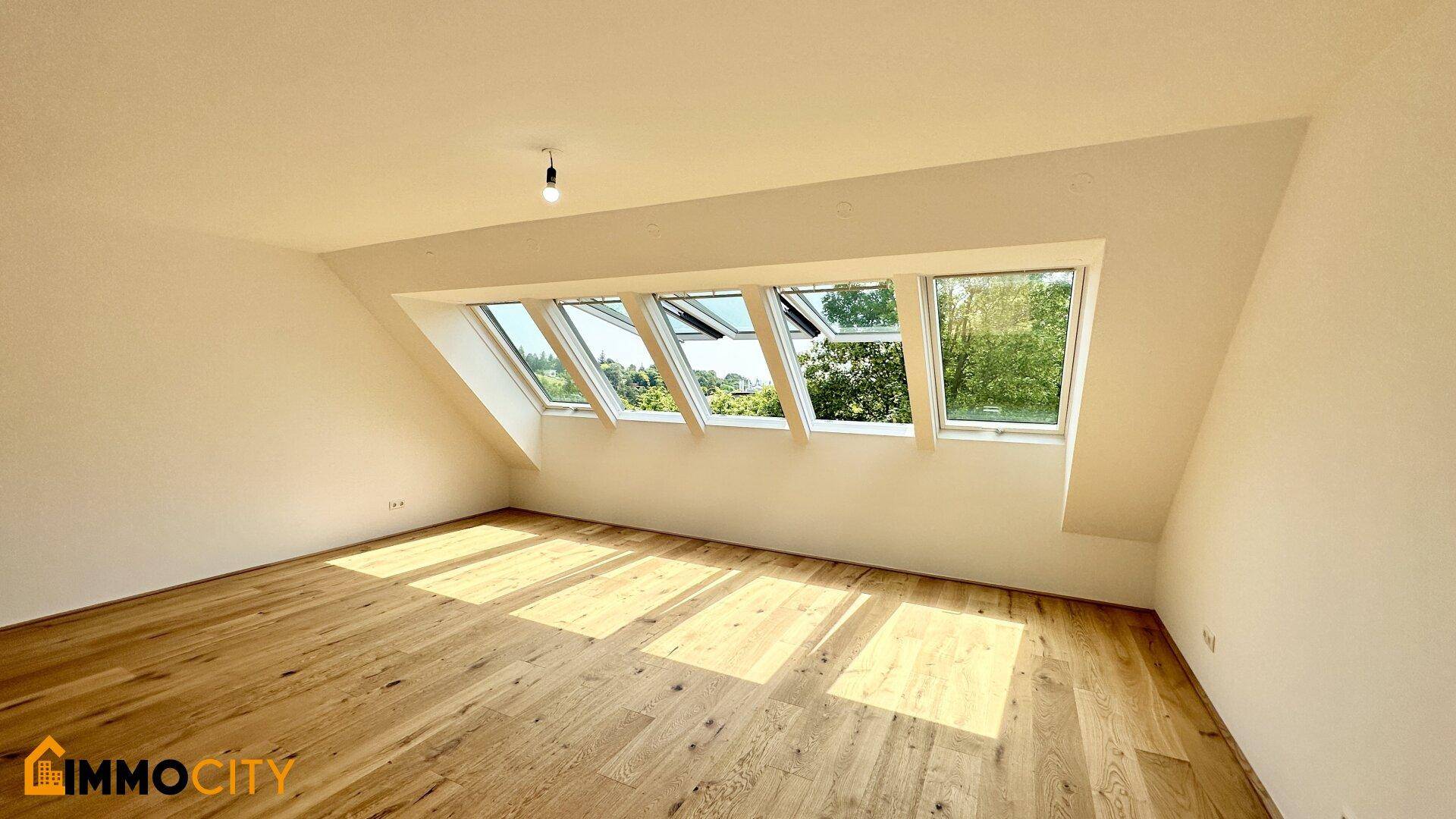 Helles Zimmer mit Holzboden und mehreren Dachfenstern, die viel Tageslicht hereinlassen.