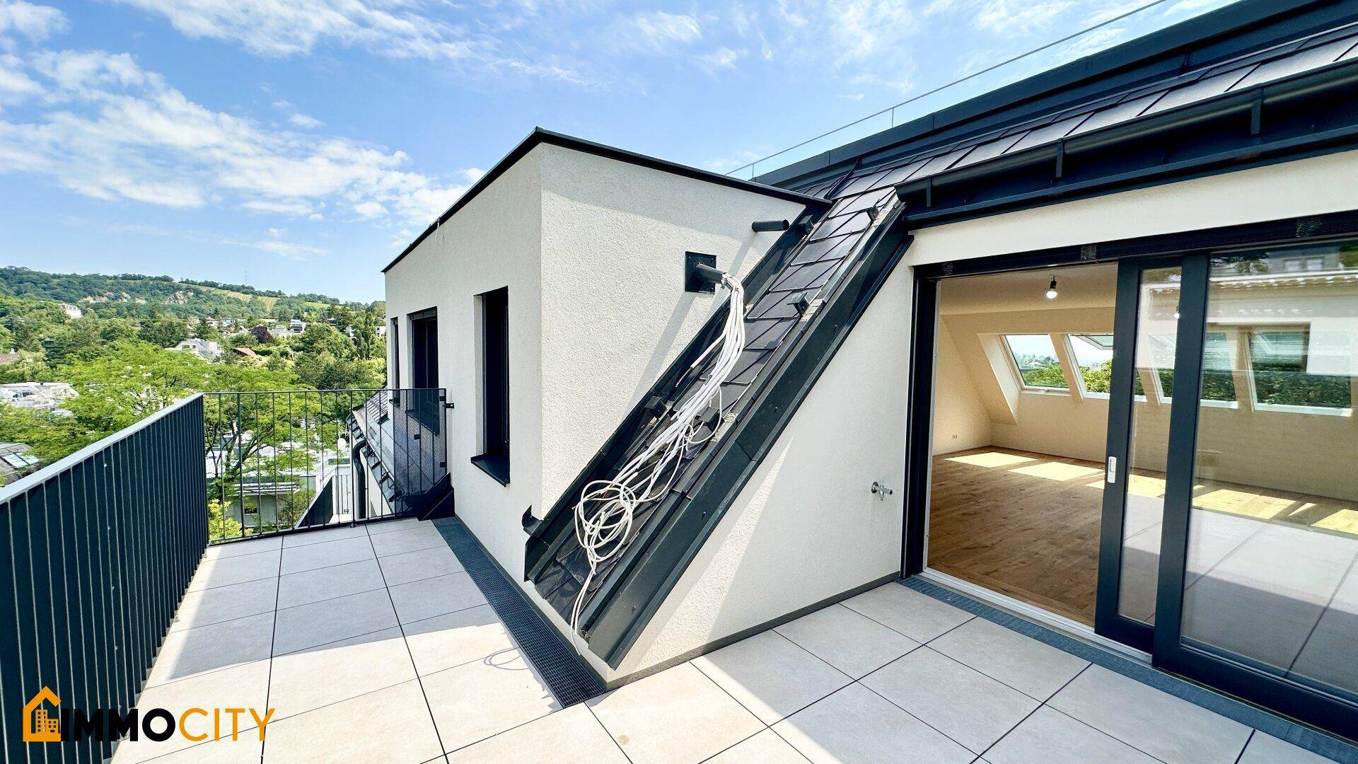 Heller Balkon mit Fliesenboden und Zugang zu einem Zimmer mit Dachfenstern und schräger Decke.