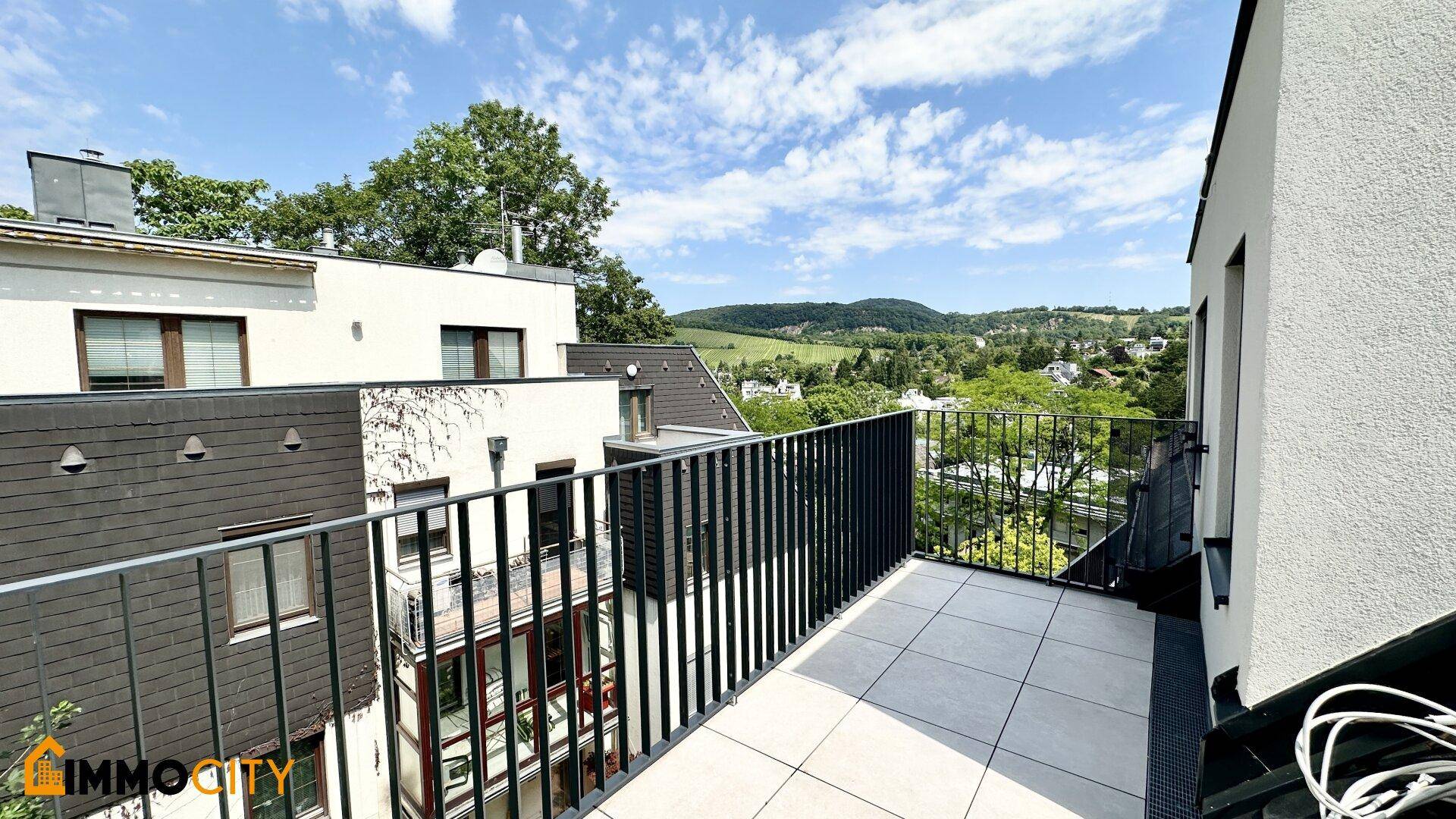 Geräumiger Balkon mit Fliesenboden und weitem Blick über die grüne Umgebung und Hügel.