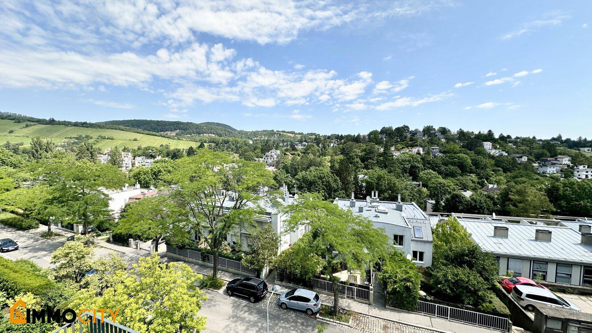 Panoramablick über eine grüne Wohngegend mit Hügeln und Bäumen unter blauem Himmel.