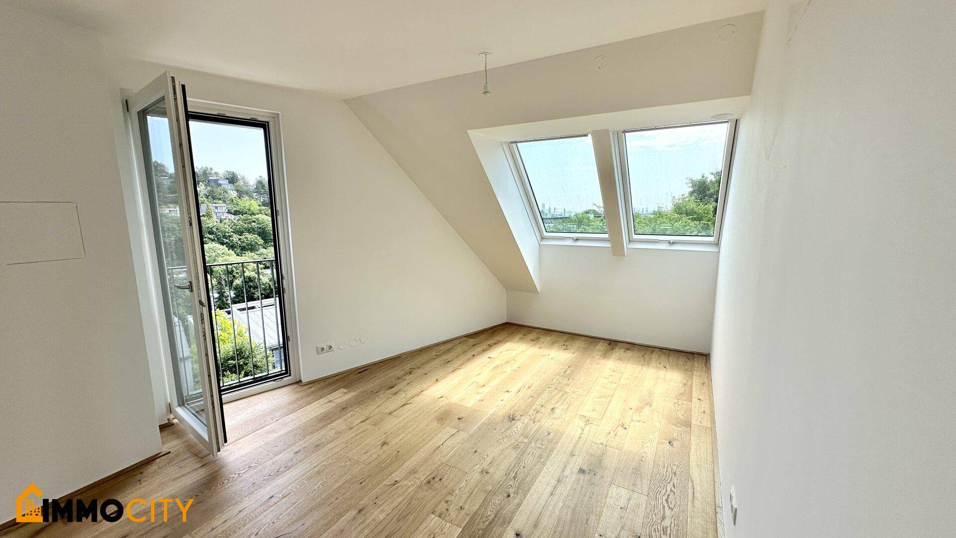 Lichtdurchflutetes Zimmer mit Holzboden, Dachfenstern und Zugang zu einem französischen Balkon.