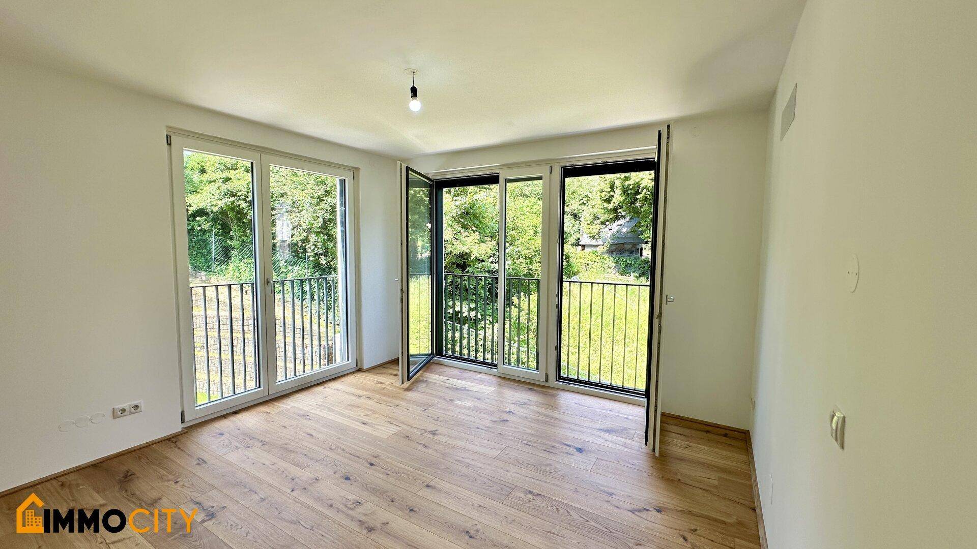 Helles Zimmer mit Holzboden und mehreren französischen Balkonen mit Blick ins Grüne.