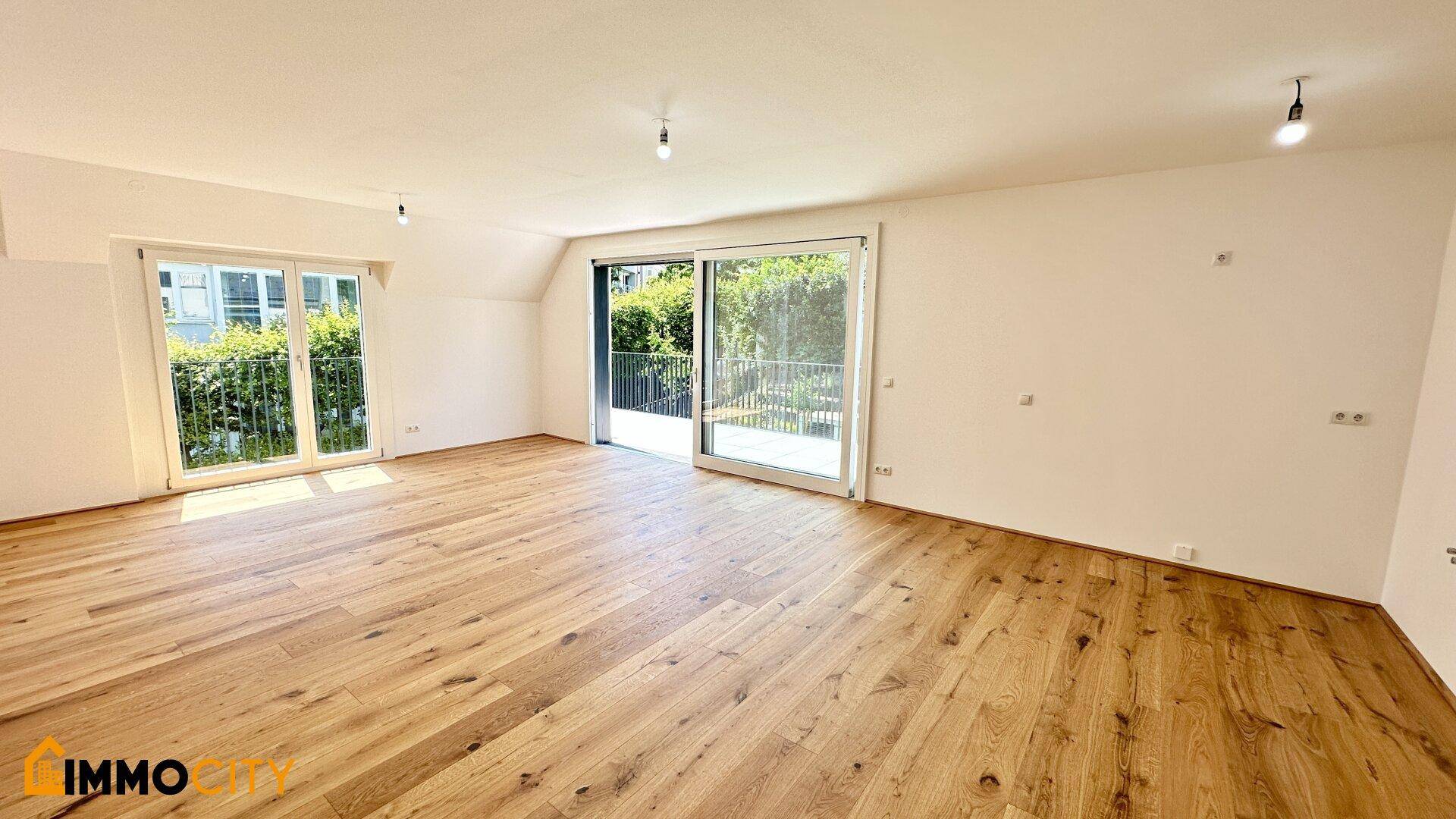 Helles, leeres Wohnzimmer mit Holzboden und großen Schiebetüren zur Terrasse.