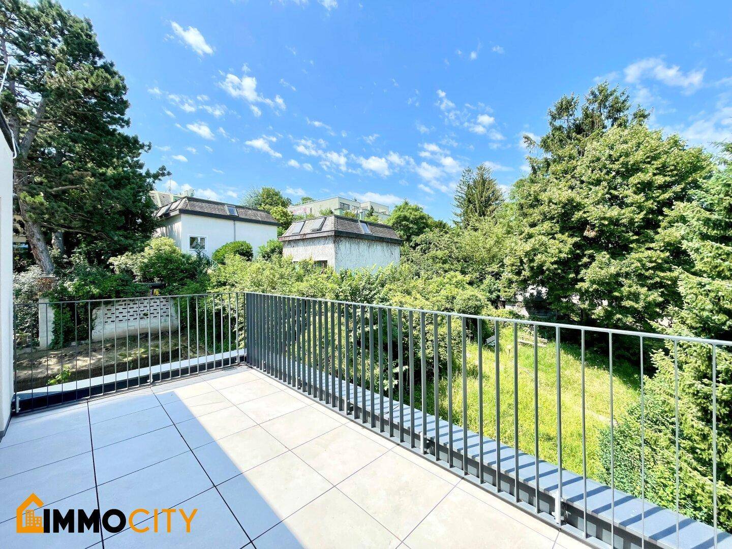 Balkon mit Fliesenboden und Metallgeländer, bietet einen ruhigen Blick auf den grünen Hinterhof mit Bäumen.