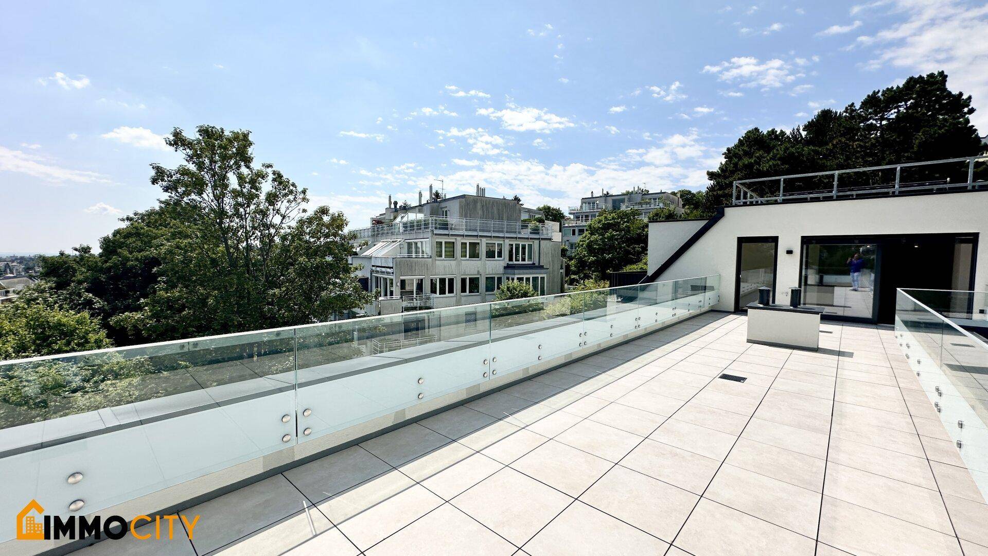 Moderne Dachterrasse mit großformatigen Fliesen und Glasgeländern, angrenzend an die Gebäudefassade.