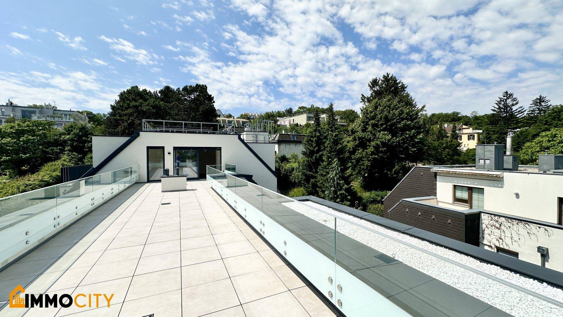 Großzügige Dachterrasse mit moderner Architektur, Glasgeländern und Blick auf umliegende Bäume.