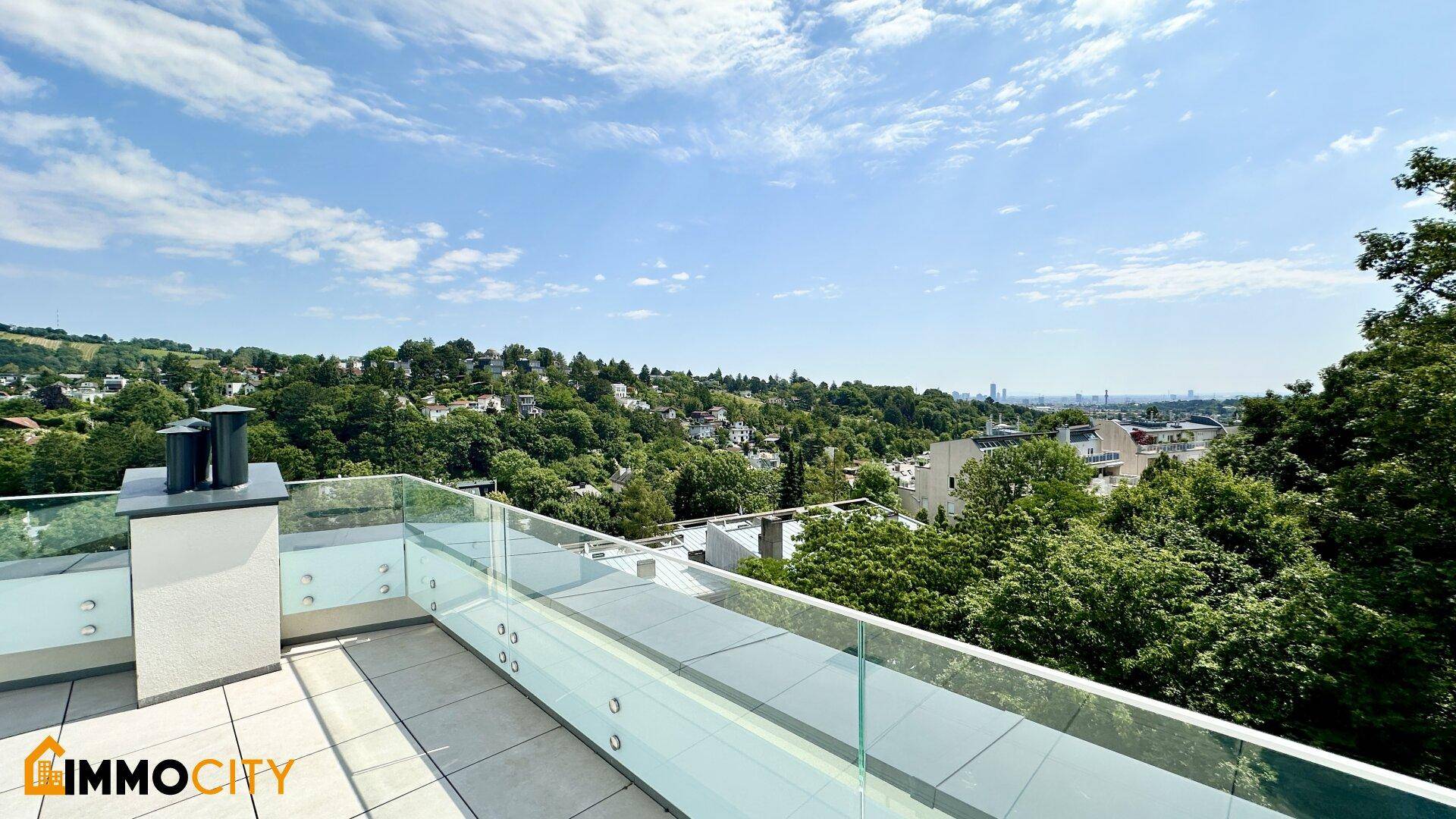 Dachterrasse mit Glasgeländer und weitem Blick über grüne Hügel bis zur entfernten Stadtkulisse.