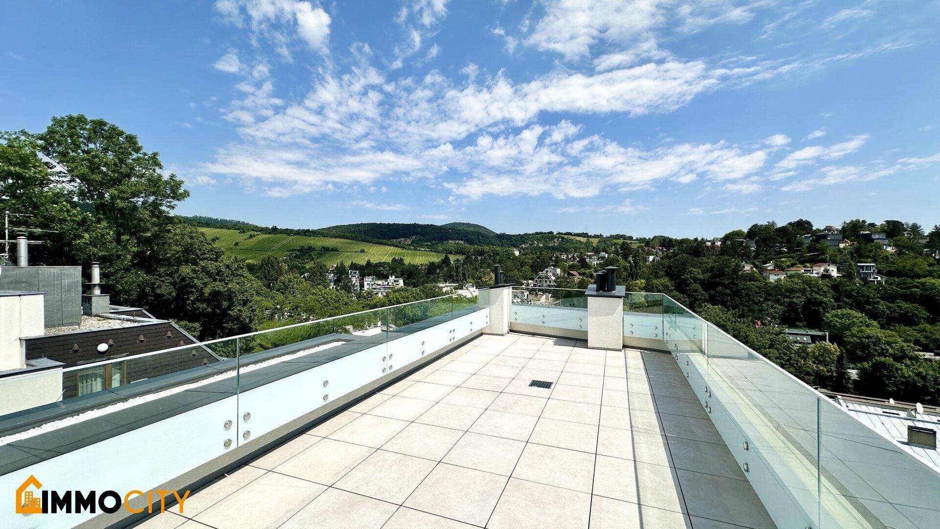 Helle Dachterrasse mit Glasbrüstung und weitem Panoramablick über die grüne, hügelige Landschaft.