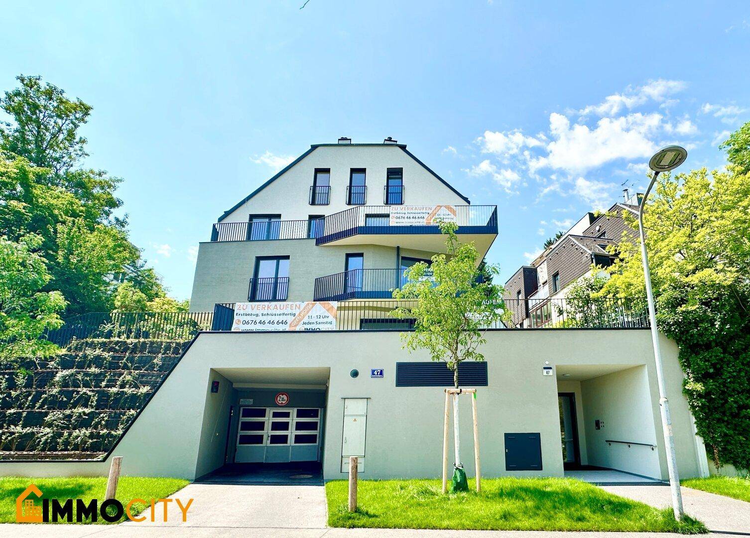 Modernes Mehrfamilienhaus mit Balkonen, Tiefgaragenzufahrt und gepflegter Außenanlage unter blauem Himmel.