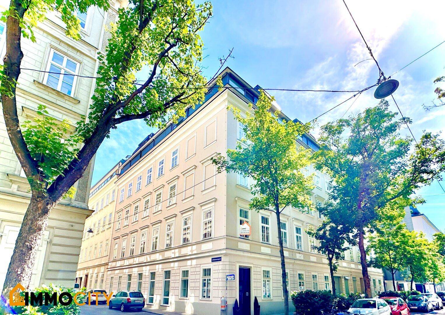 Historisches Eckgebäude mit klassischer Architektur und vielen Fenstern in einer sonnigen Stadtlage.