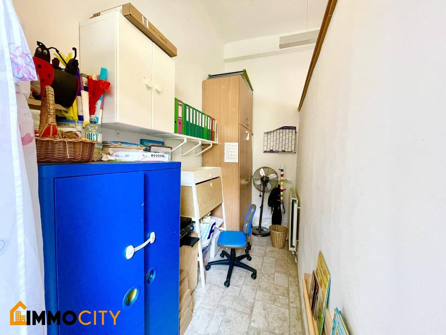 Kleiner Abstellraum oder Büro mit Regalen, einem blauen Schrank und einem Ventilator.