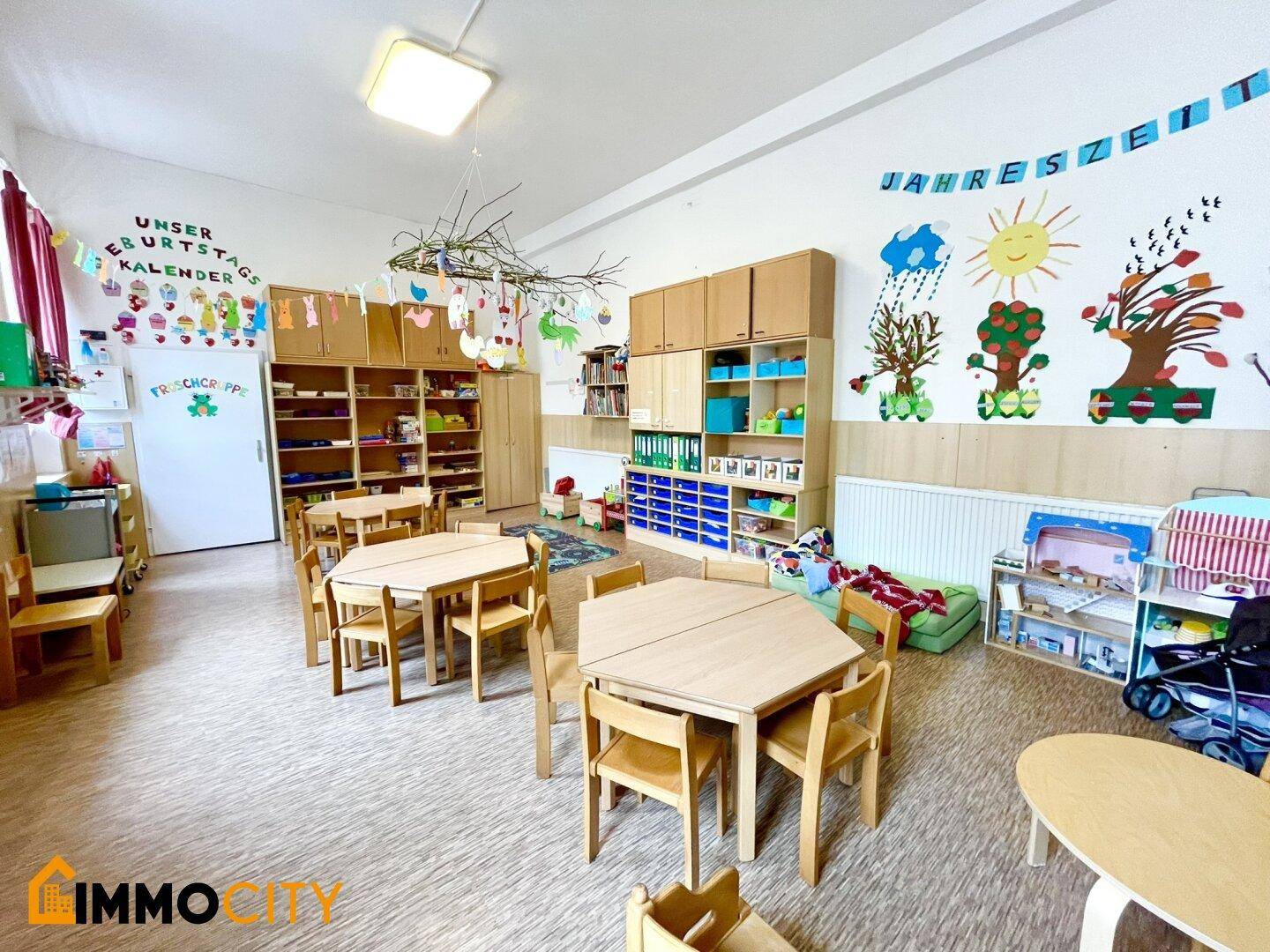 Helles Klassenzimmer mit Kindermöbeln, vielen Regalen und pädagogischen Wanddekorationen.