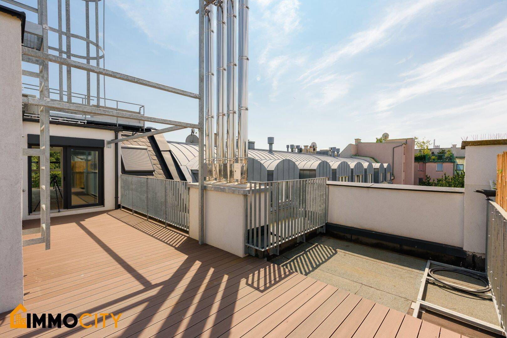 Dachterrasse mit Holzboden, Metallgeländer und Zugang zum Innenbereich des Gebäudes.