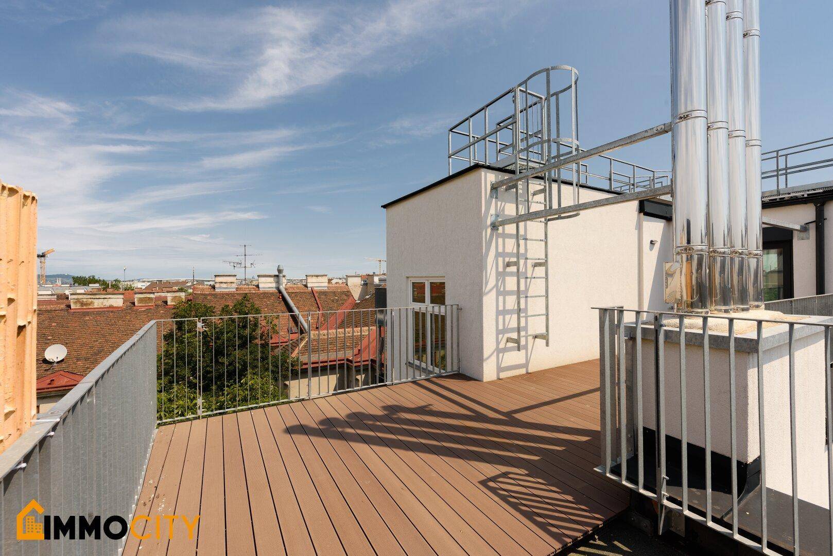 Dachterrasse mit Zugang zu einem kleinen Gebäude und Blick auf die umliegenden Dächer.