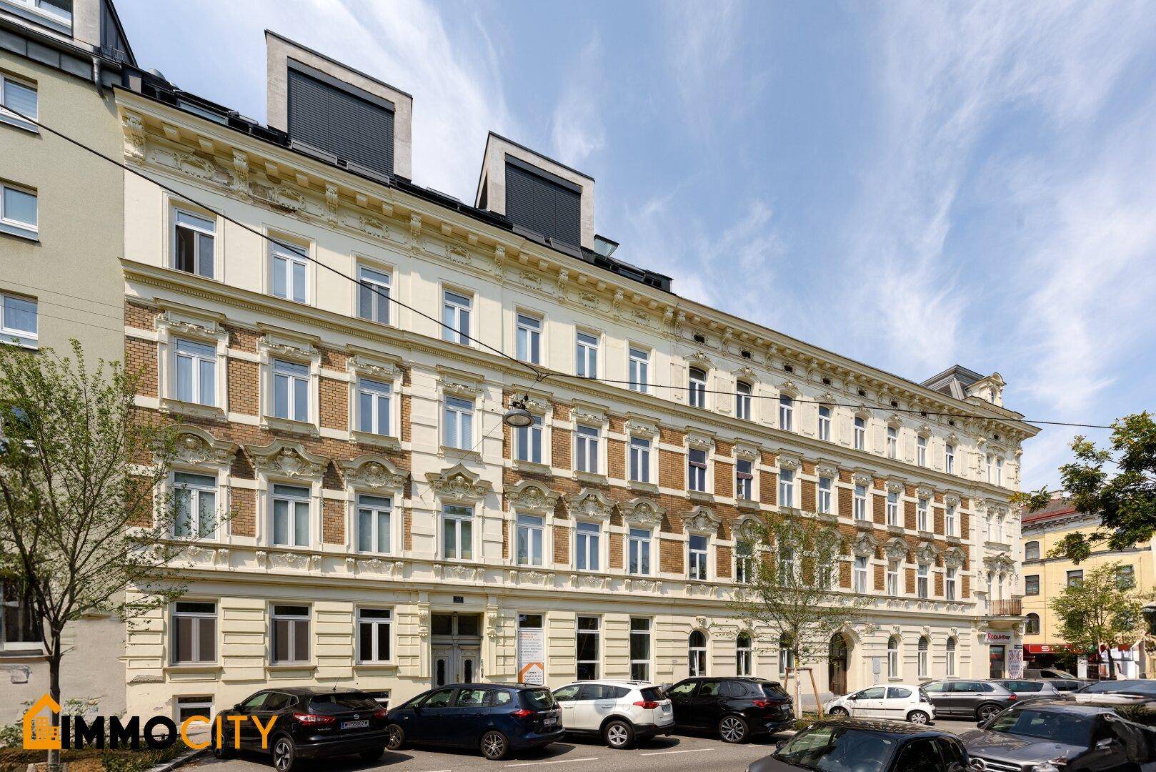 Historisches Gebäude mit detailreicher Fassade, vielen Fenstern und geparkten Autos davor.