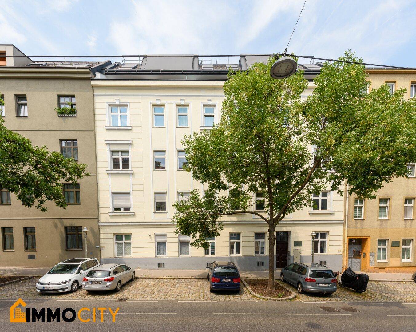 Klassische Fassade eines Mehrfamilienhauses mit parkenden Autos und Bäumen davor.