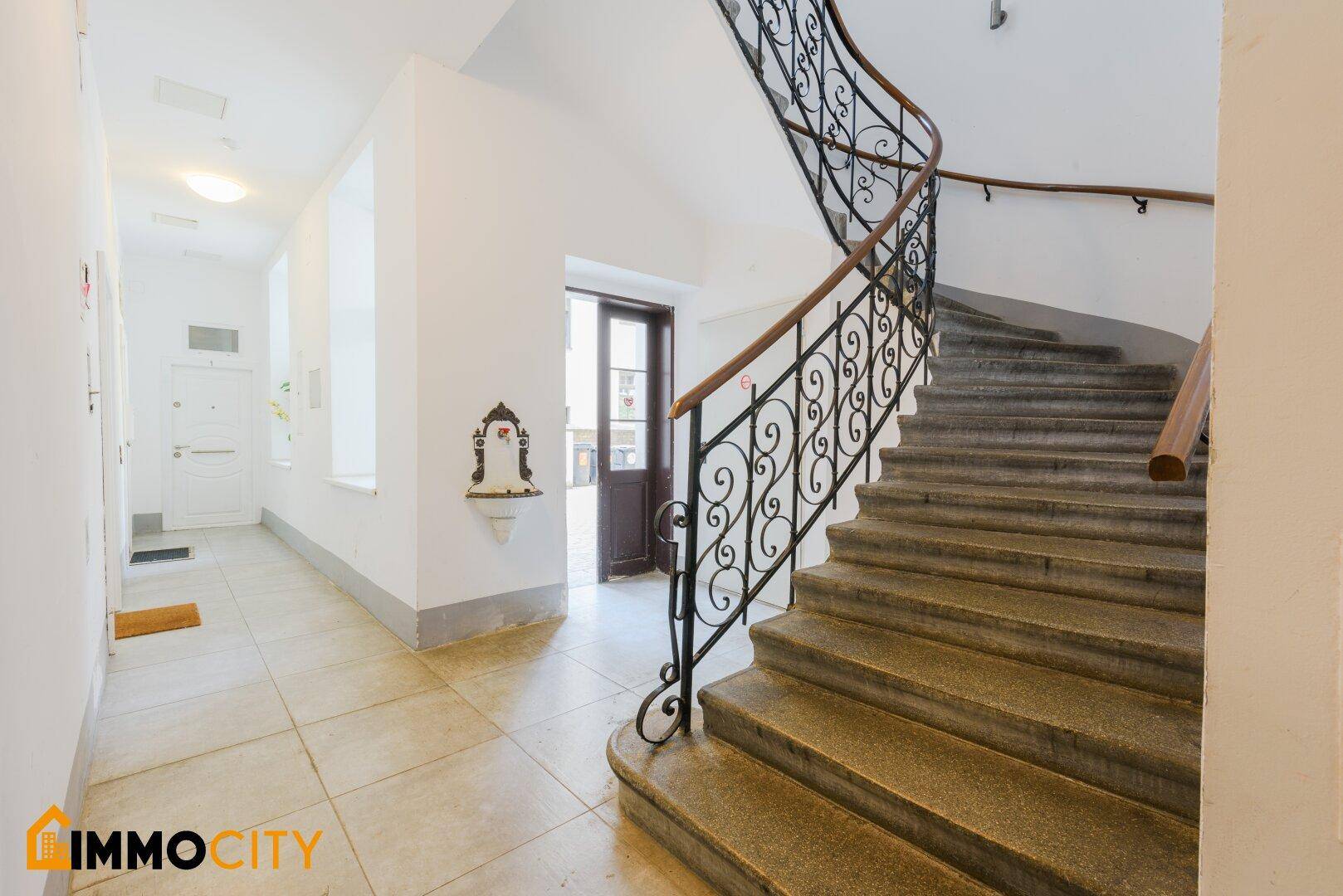 Elegantes Treppenhaus mit schmiedeeisernem Geländer und Steinstufen in einem Altbau.