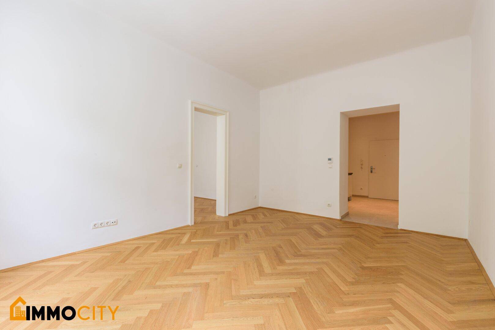 Helles Zimmer mit Fischgrätparkettboden und weißen Wänden, bereit zur individuellen Gestaltung.
