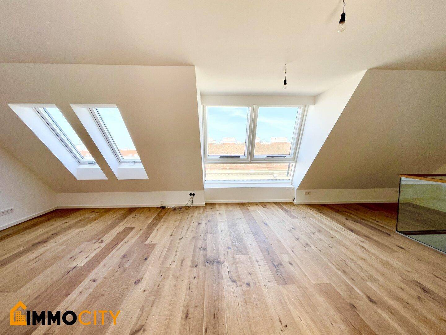 Heller Dachbodenraum mit Holzboden, schrägen Decken und mehreren Dachfenstern.