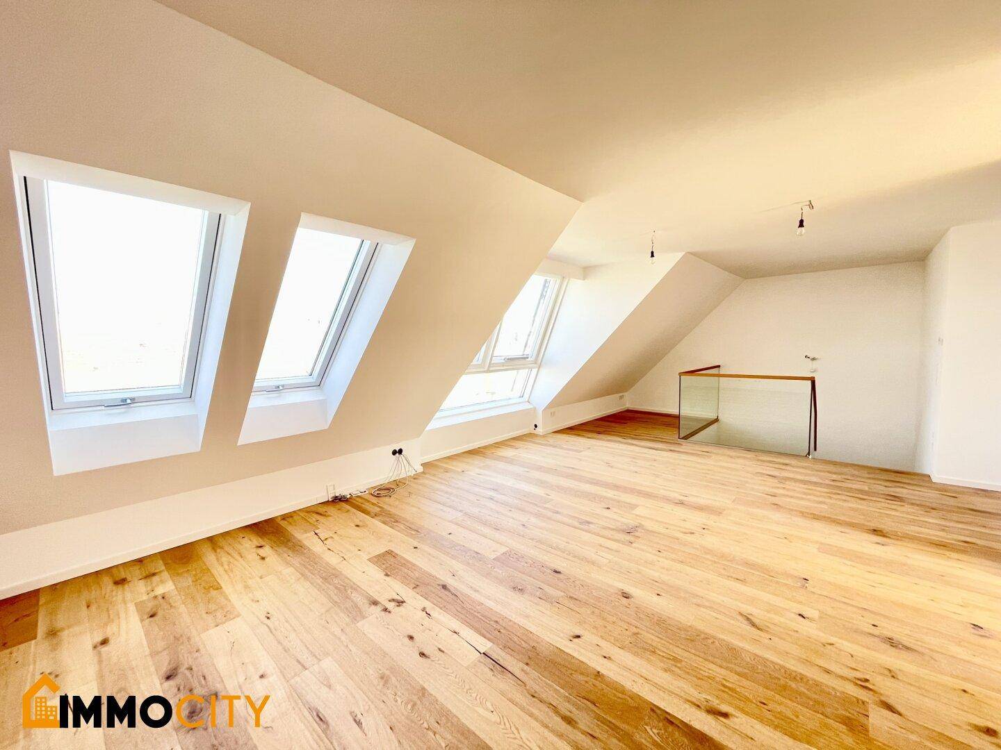 Heller Dachbodenraum mit Holzboden, schrägen Decken und mehreren Dachfenstern.