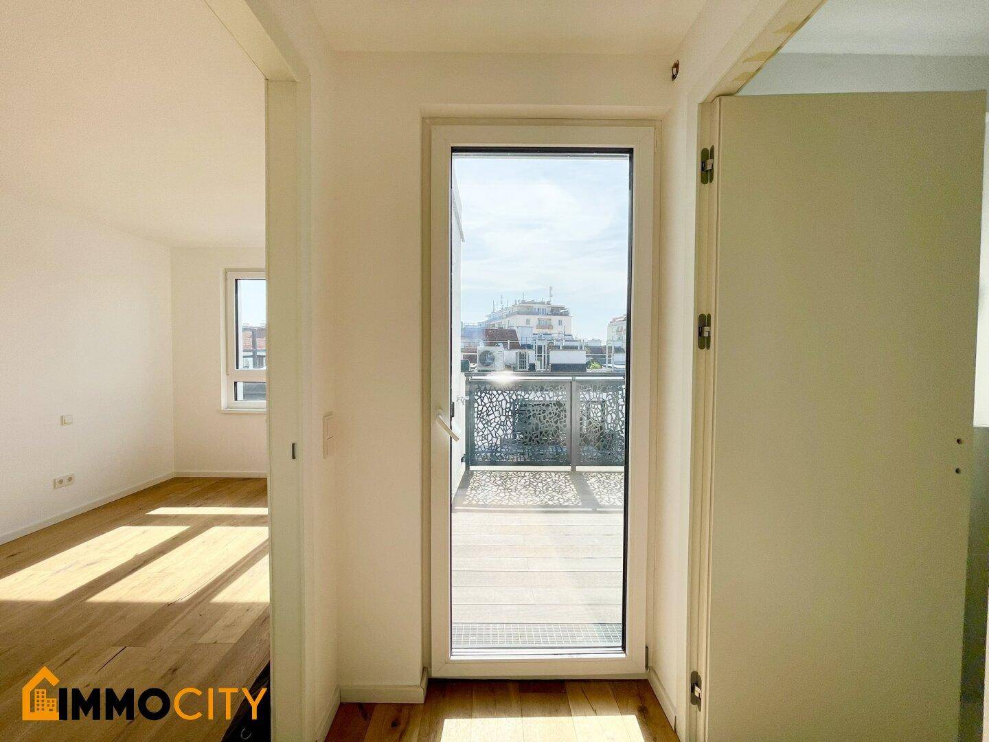 Eingangsbereich mit Holzboden und Tür, die zu einer sonnigen Dachterrasse führt.