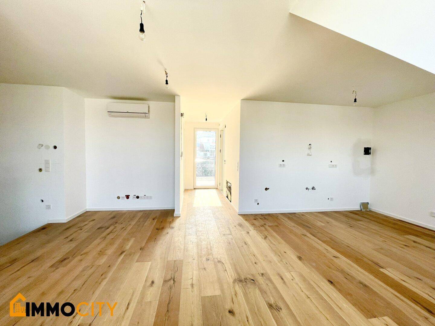 Heller Raum mit Holzboden, Klimaanlage und Zugang zu einem sonnigen Außenbereich.