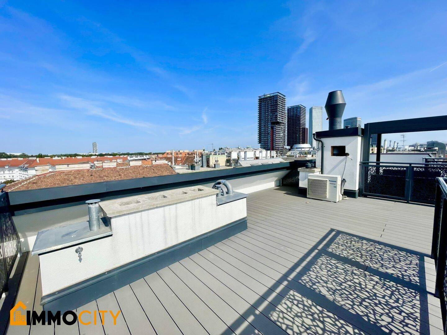 Weitläufige Dachterrasse mit Holzboden, Stadtblick und modernen Hochhäusern im Hintergrund.