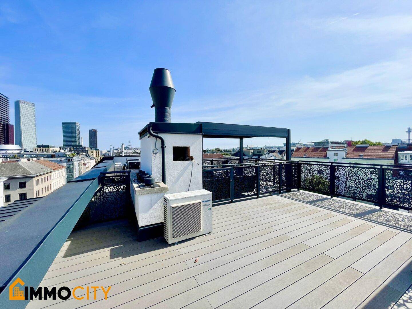 Weitläufige Dachterrasse mit Holzboden, Stadtblick und modernen Hochhäusern im Hintergrund.