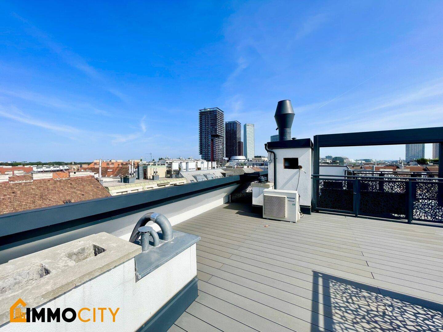 Weitläufige Dachterrasse mit Holzboden, Stadtblick und modernen Hochhäusern im Hintergrund.