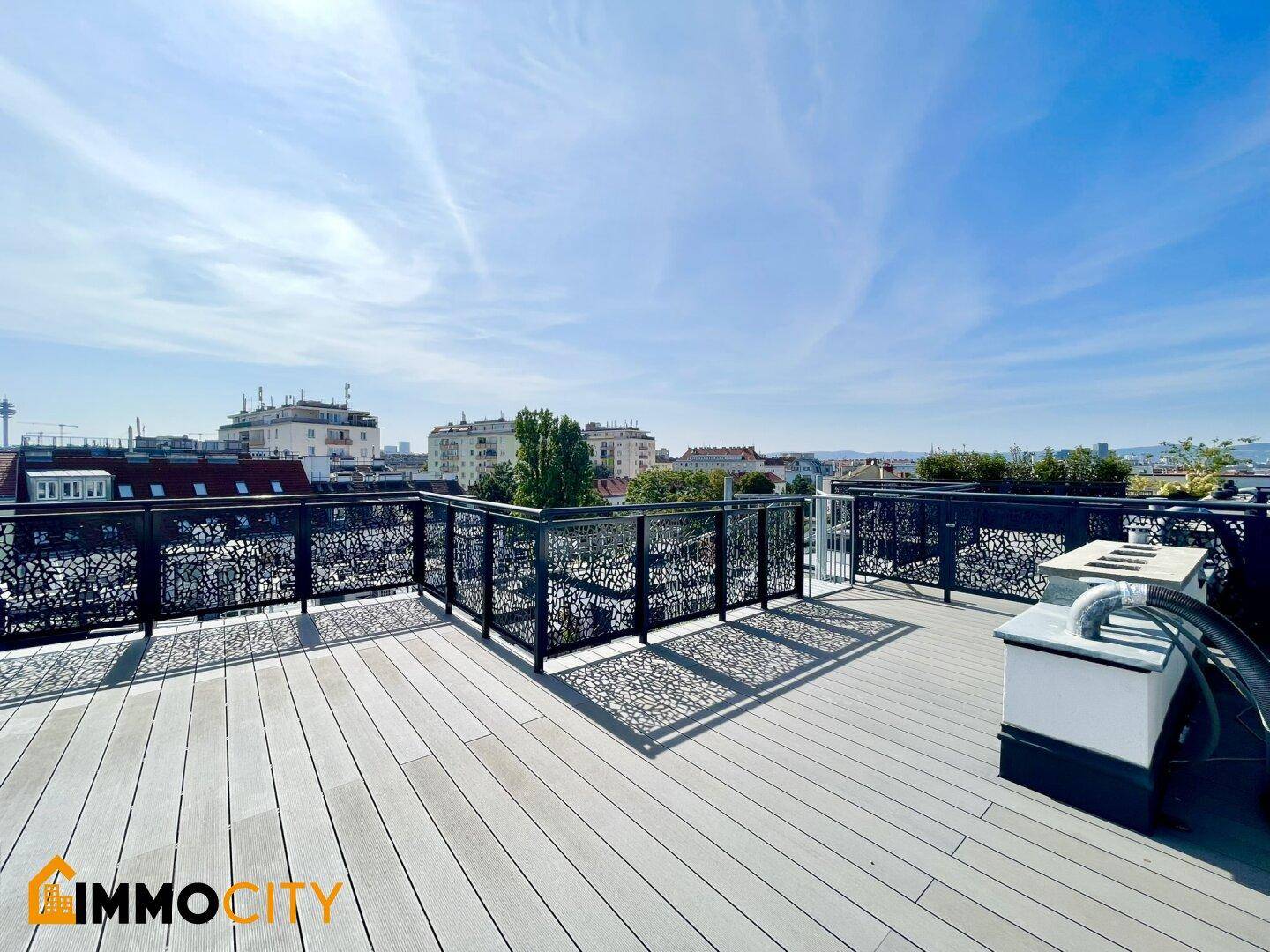 Weitläufige Dachterrasse mit Holzboden, modernem Geländer und Panoramablick über die Stadt.
