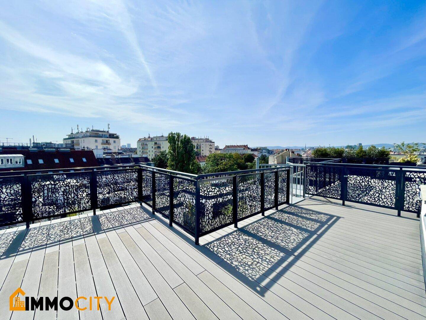 Große Dachterrasse mit Holzboden, dekorativem Geländer und weitem Stadtblick unter blauem Himmel.